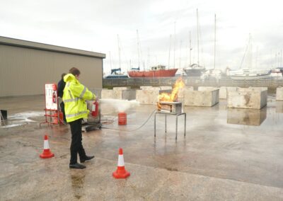 Trainee using a fire extinguisher on a controlled fire outdoors